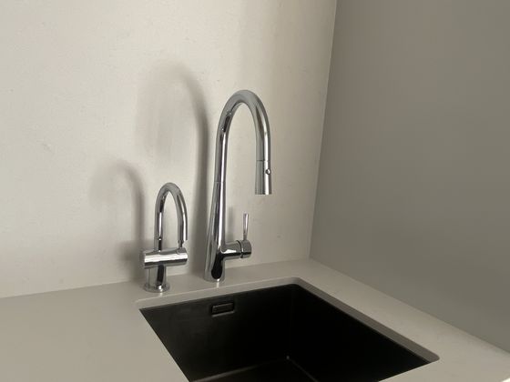 A separate slim drinking water tap beside the main pull-down mixer at an undermount kitchen sink, set in a pale stone benchtop.