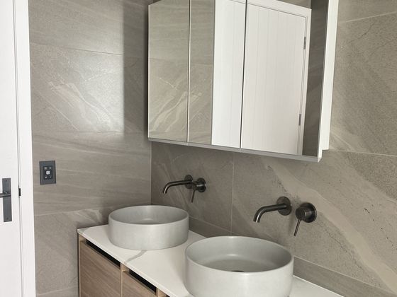 Twin stone vessel basins on a timber vanity with two black wall-mounted mixers, under a mirrored wall cabinet.