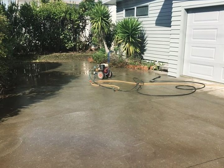 Water lying across a concrete driveway beside a garage door, with a hose and a pump set up to clear it.