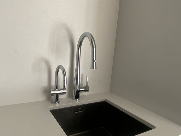 A separate slim drinking water tap standing beside the main pull-down mixer at an undermount kitchen sink, on a pale stone benchtop.